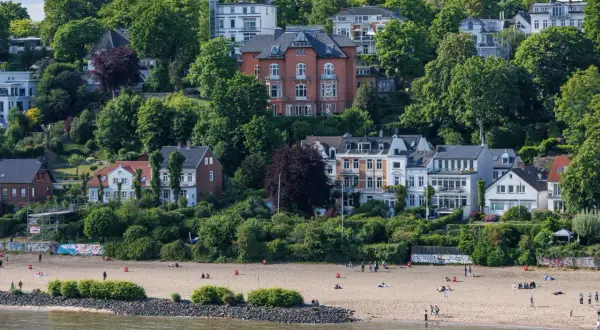 Prächtige Villen und grüne Hügel über einem Sandstrand an den Elbvororten Hamburgs. Menschen genießen den sonnigen Tag am Wasser.