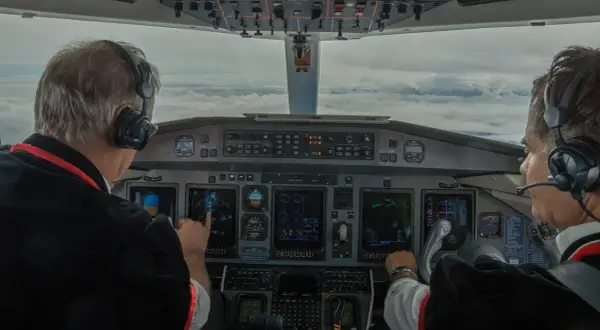 Dwóch pilotów w kokpicie, jeden wskazuje na ekran. Zastanawiasz się, ile zarabia pilot? To praca pełna odpowiedzialności.