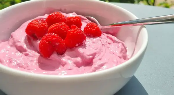 En skål med rosa krämig dessert toppad med färska hallon. Perfekt för nyttiga snacks en solig dag.