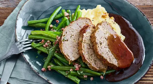 Saftiger hackbraten im ofen, serviert mit grünen Bohnen und Kartoffelpüree, übergossen mit dunkler Soße.