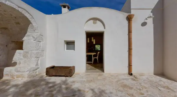 Interni di trulli pugliesi: un'apertura bianca rivela una sala da pranzo accogliente, con un camino e un piccolo orto in pietra all'esterno.