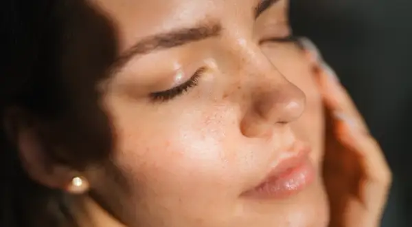 Viso di donna con lentiggini, illuminato da luce soffusa. La pelle appare curata, suggerendo che retinolo e vitamina C si possono usare insieme per un incarnato radioso.