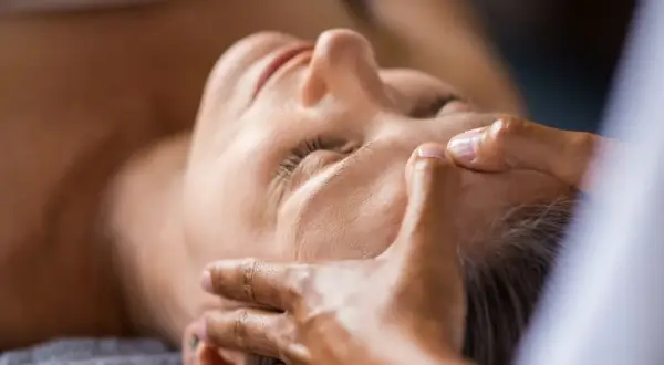 Mani esperte dimostrano come massaggiare il viso per le rughe, con un tocco delicato sulla fronte e sulle tempie per un effetto rilassante e ringiovanente.
