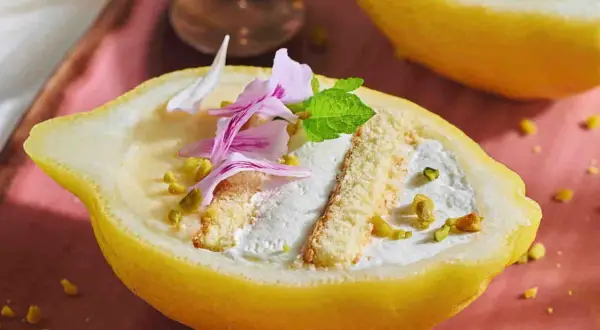 Delizia al limone: crema soffice e biscotti in un limone scavato, guarnito con pistacchi e petali rosa.