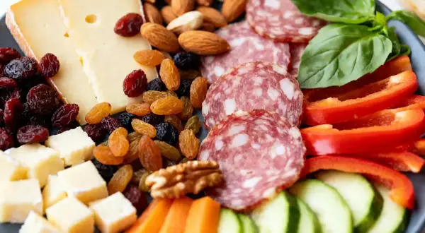 Une délicieuse planche apéro fromage avec salami, fruits secs, noix, poivrons rouges, concombres et carottes. Parfait pour un moment convivial.