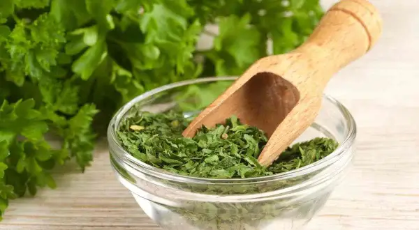 Prezzemolo essiccato in una ciotola di vetro, con un mestolo di legno. Un'erba aromatica utile anche in gravidanza.