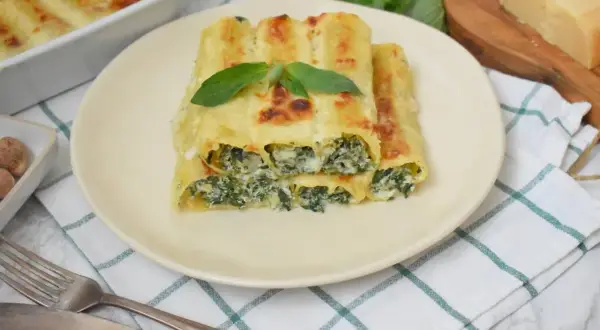Pyszne cannelloni ze szpinakiem, zapieczone pod beszamelem i serem, ozdobione listkiem bazylii.