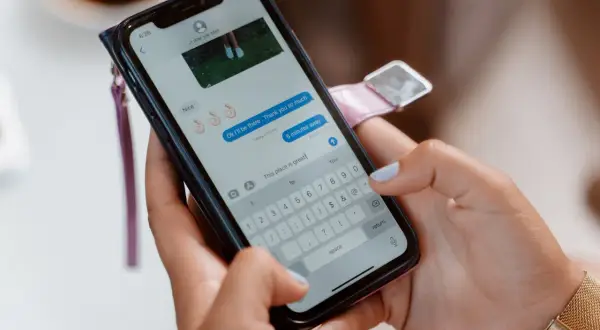 Dłonie trzymające smartfon, na ekranie czat Messenger. Zastanawiasz się, jak włączyć gry na Messengerze?