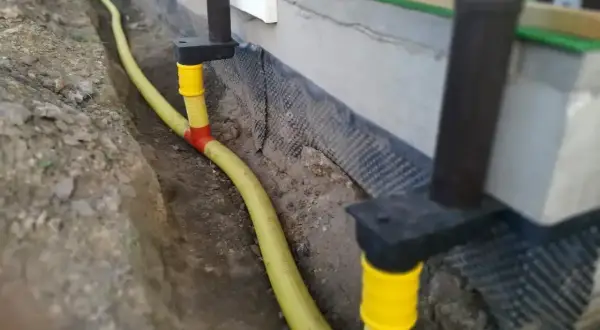 System odprowadzenia wody z rynny, z żółtą rurą biegnącą w wykopie przy fundamencie.