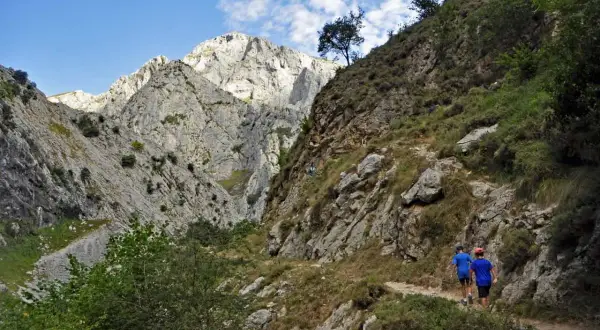 Dos niños disfrutan de la ruta Poncebos - Bulnes con niños, caminando por un sendero rocoso entre imponentes montañas.