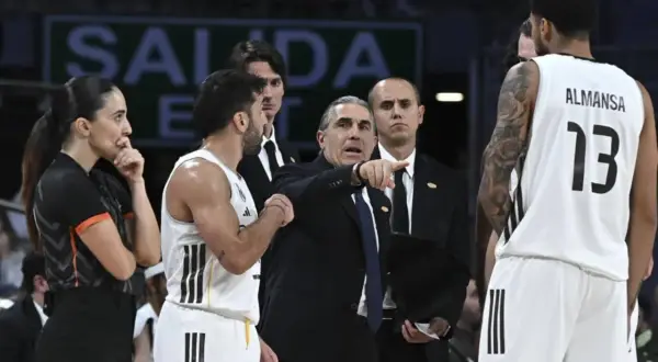 Entrenador del r madrid baloncesto señala una jugada. Jugadores y árbitra observan.
