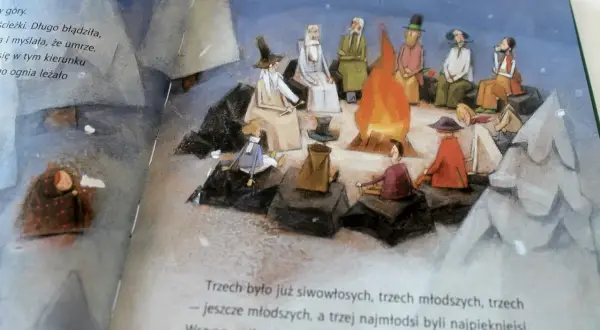 Ilustracja przedstawia grupę ludzi siedzących wokół ogniska, z dzieckiem przykrytym kocem po lewej stronie.