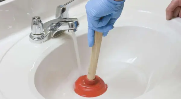 Main tenant utilise une ventouse pour déboucher un lavabo. L'eau s'accumule, signe d'un lavabo bouché.