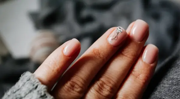 Une main aux ongles rose pâle, avec une délicate méduse dessinée sur l'annulaire. Une manucure pastel subtile et élégante.