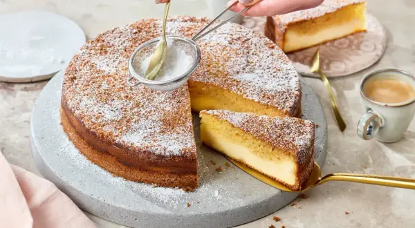 Ein köstlicher Kuchen mit Puderzucker wird bestäubt. Ein Stück wird mit einem goldenen Tortenheber herausgehoben. Dreh dich um, Kuchen, du siehst lecker aus!