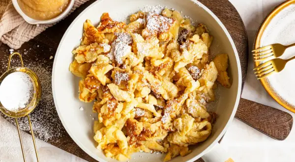 Kaiserschmarrn ohne Ei, fluffig und goldbraun, mit Puderzucker bestäubt. Dazu Apfelmus und zwei Gabeln.