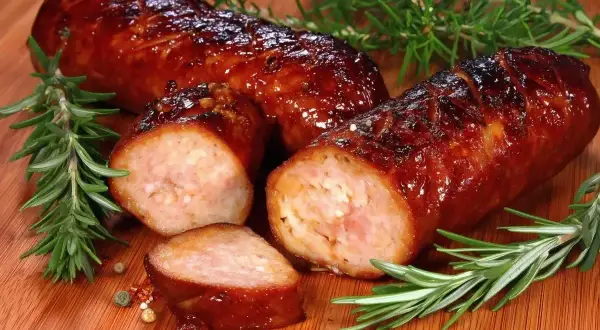 Soczysta kiełbasa z piekarnika, rumiana i aromatyczna, z gałązkami rozmarynu i ziarnami pieprzu na desce.