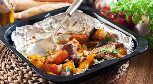 Szybkie danie z piekarnika: pieczone warzywa korzeniowe, dynia i mięso w folii aluminiowej, gotowe do podania.