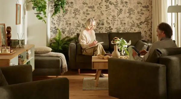 Przytulny salon, idealny, by pokazać, jak urządzić pokój dla babci. Starsza pani pisze, piesek czuwa.