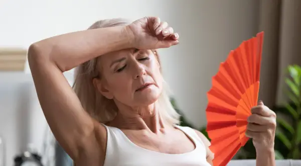 Frau fächelt sich mit einem orangefarbenen Fächer Luft zu, um etwas gegen Hitzewallungen zu tun.