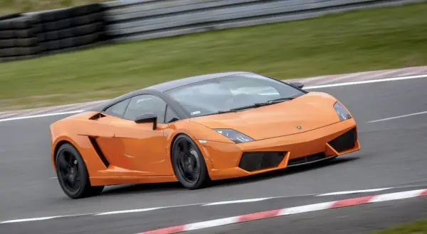 Pomarańczowe Lamborghini pędzi po torze wyścigowym, zostawiając za sobą smugę prędkości.