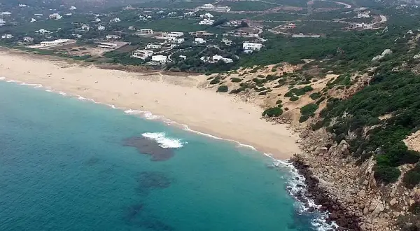 Vista aérea de la playa de los alemanes en Foz, con casas blancas dispersas entre la vegetación y el mar turquesa.