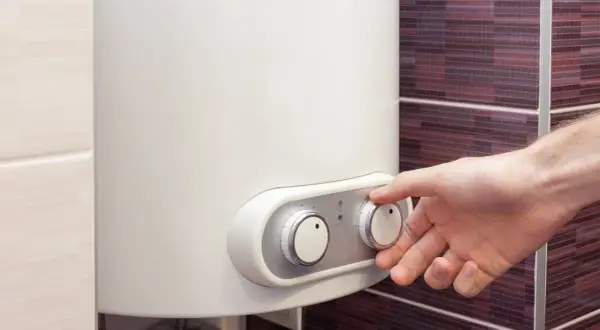 Dłoń reguluje pokrętłem mały bojler elektryczny. Wskaźnik "ON" świeci na zielono.