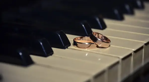Dos alianzas de oro descansan sobre teclas de piano, evocando la pregunta: ¿cuanto pesa una alianza de oro?