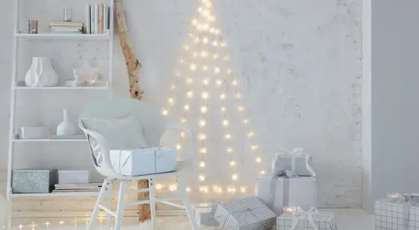 Eine Lichterkette an der Decke befestigt, bildet einen Weihnachtsbaum. Geschenke und ein Stuhl stehen davor.
