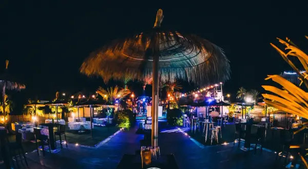 Noche vibrante en el chiringuito Macenas. Sombrillas de paja, luces de colores y mesas listas para disfrutar.