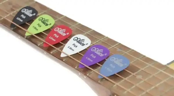 Kolorowe kostki do gry na gitarze Alice leżą na strunach. Każda kostka ma inny kolor i grubość.
