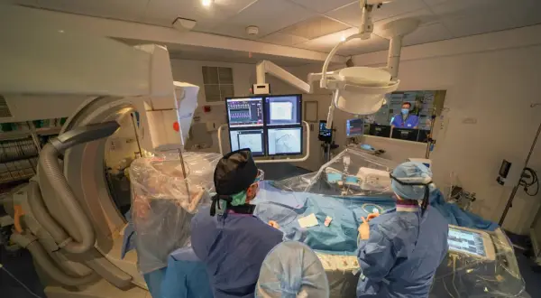 Équipe médicale en salle d'angiographie, préparant le repos après une coronarographie. Moniteurs affichant des images cardiaques.