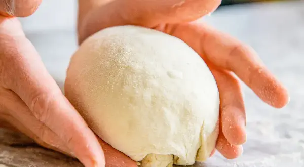 Hände formen einen Teigball auf einer bemehlten Oberfläche.