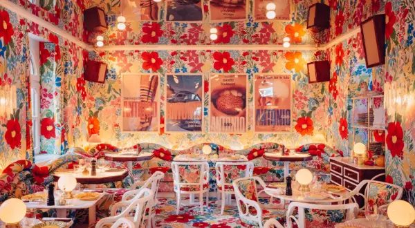 Ein Restaurant mit floralem Muster an Wänden, Boden und Möbeln, Tische sind gedeckt.
