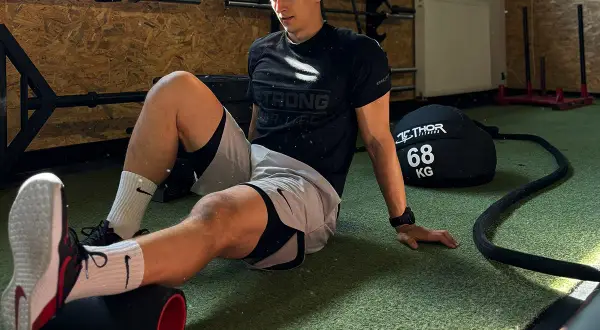 Mężczyzna na siłowni roluje mięśnie na wałku. To część treningu, który może być związany z metcon crossfit, co to znaczy intensywny wysiłek.
