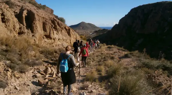 Grupo de excursionistas disfrutando de una randonnée en Cabo de Gata, con el mar y un volcán al fondo.