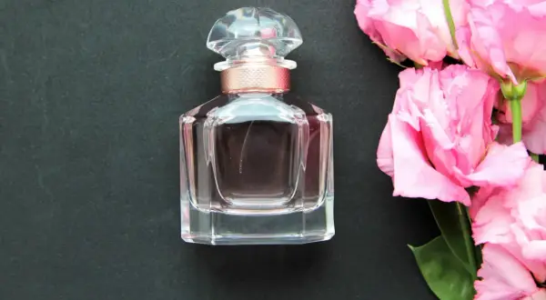 Elegancka buteleczka wody toaletowej obok bukietu różowych kwiatów. Wybór między wodą toaletową a wodą perfumowaną zależy od preferencji.
