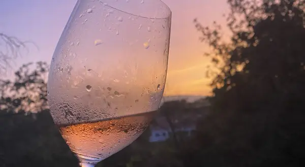 Calice di vino rosato, con gocce di condensa, al tramonto. Un brindisi alla vinificazione in rosato.