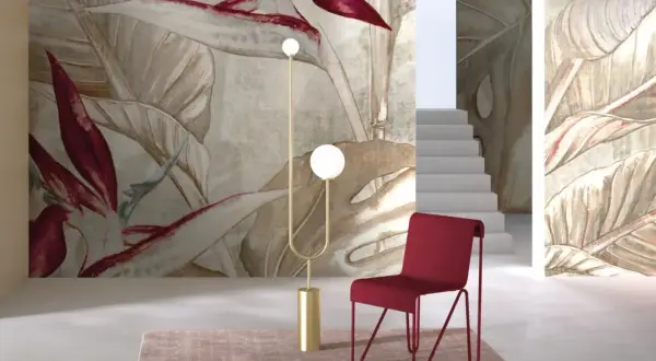 Egzotyczne, drogie tapety z motywem liści i kwiatów tworzą luksusową atmosferę. Czerwone krzesło i złota lampa dodają elegancji.