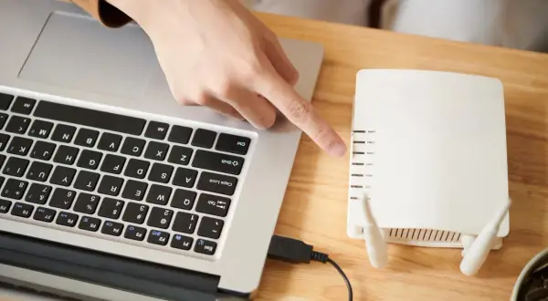 Ręka wskazuje na router, podłączony kablem USB do laptopa. Dowiedz się, jak połączyć falownik z wifi.