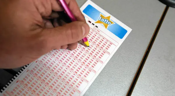 Ręka z różowym ołówkiem zaznacza liczby na kuponie Lotto, być może to właśnie tutaj padną wygrane.