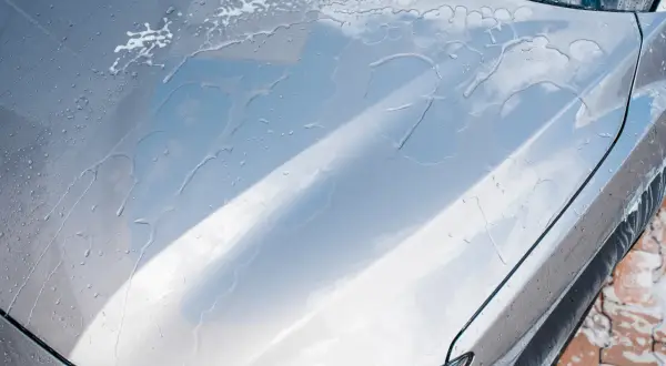 Krople wody i piany na masce srebrnego auta. Czy po woskowaniu płukać auto? Tak, aby uzyskać idealny połysk.