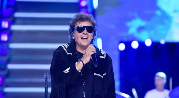 Janusz Panasewicz w czarnej kurtce z frędzlami i okularach przeciwsłonecznych śpiewa na scenie.