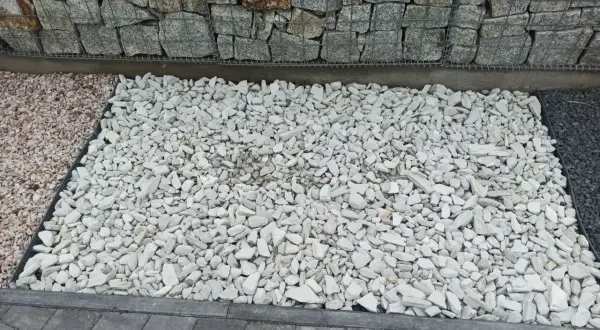 Biały grys, czyli drobne, łamane kamienie, tworzy jasną powierzchnię obok gabionów i ciemniejszego kamienia.
