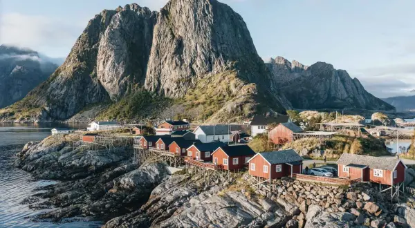 Village de pêcheurs aux maisons rouges sur pilotis, dominant la mer, avec une montagne imposante en arrière-plan. Idéal pour un circuit Lofoten 6 jours.