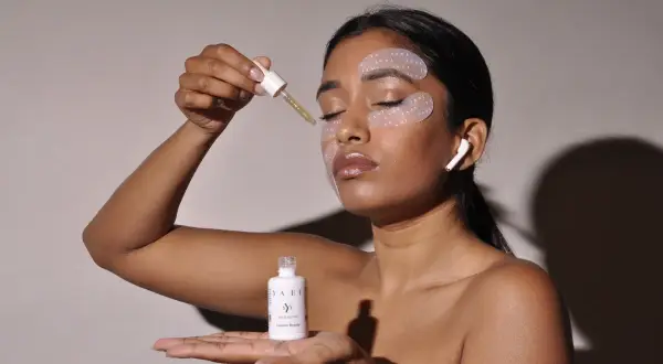 Donna applica siero per il contorno occhi disidratato. Patch idratanti e auricolari completano il rituale di bellezza.