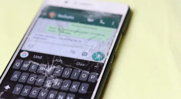 Pęknięty ekran telefonu wymaga pilnej wymiany. Widać klawiaturę i fragmenty rozmowy.