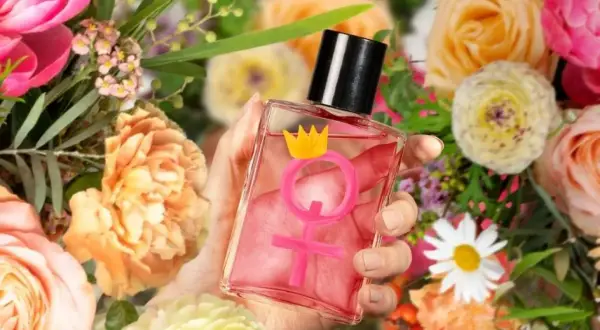 Dłoń trzyma flakonik z różowym płynem i symbolem Wenus zwieńczonym koroną. Czy perfumy z feromonami działają? Otoczenie bujnych kwiatów sugeruje zapach.