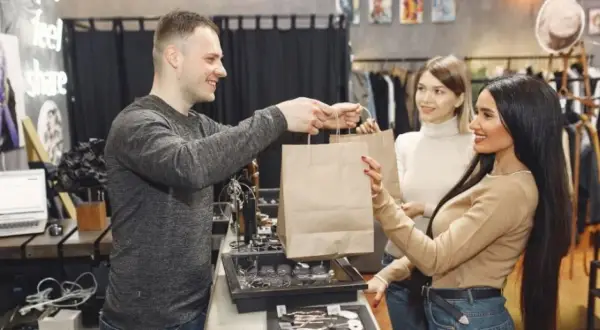 Hombre entrega bolsas de compras a dos mujeres en una tienda.