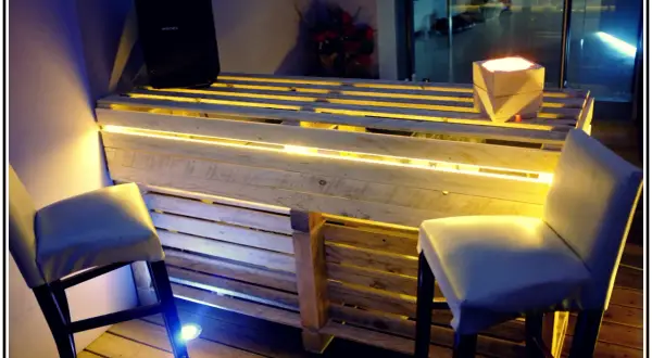Bancone bar fai da te con pallet, illuminazione a LED e sgabelli. Un'idea creativa per un angolo bar moderno.
